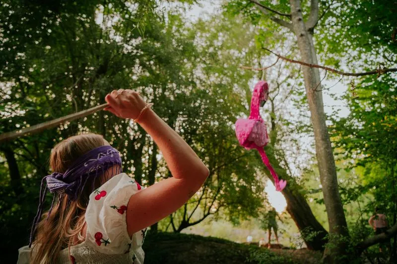Frau mit Augenbinde holt zum Schlag auf eine Flamingo-Piñata aus