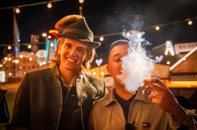 Zwei Freunde im Festzelt, einer bläst eine Rauchwolke aus